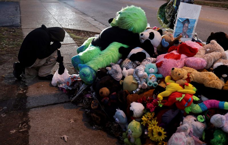 A protester kneels next to a memorial in the middle of the street, Monday, Nov. 24, 2014, more than three months after a black 18-year-old man was shot and killed there by a white policeman in Ferguson, Mo. 