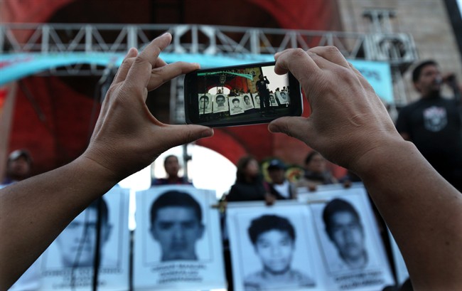 A protester takes a photo of the relatives of 43 missing students from the Isidro Burgos rural teachers college standing on a stage during a protest in Mexico City, Saturday, Dec. 6, 2014. 