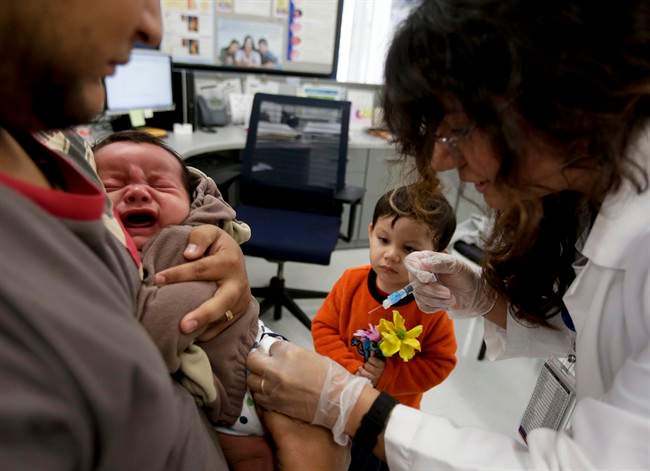 FILE- In this Dec. 10, 2014, file photo, Julietta Losoyo, right, a registered nurse at the San Diego Public Health Center gives Derek Lucero a whooping cough injection while in his fathers Leonel's arms as his brother Iker, 2, looks on.