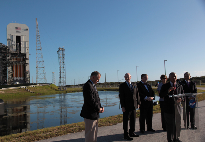 NASA administrator Charles Bolden, at the podium, speaks to the media in front of ULA’s Delta IV Heavy rocket with Orion atop.