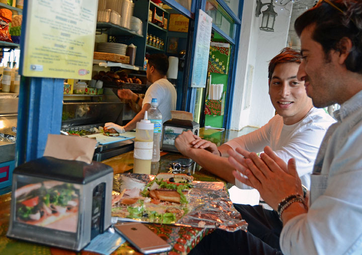 This Nov. 3, 2014 photo shows Julian Cohen, right, of Miami Beach, and friend Ryan Salomon, of New York, trying the sandwiches at La Sandwicherie, in Miami Beach, Fla., a highlight of South Beach's side streets where travelers will find inexpensive local favorites for food, accommodations and souvenirs.
