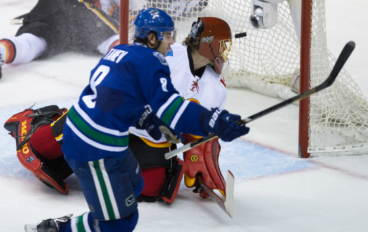 Vancouver Canucks' Chris Tanev, left, scores the winning goal against Calgary Flames' goalie Jonas Hiller, of Sweden, during the overtime period of an NHL hockey game in Vancouver, B.C., on Saturday December 20, 2014.