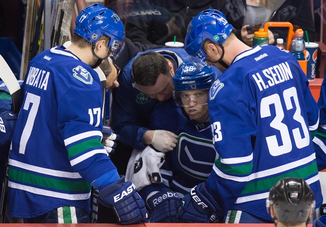 Vancouver Canucks' Jannik Hansen, centre, of Denmark, is tended to by a trainer as Radim Vrbata, of the Czech Republic, and Henrik Sedin, of Sweden, watch after he was checked during the second period of an NHL hockey game against the Calgary Flames in Vancouver, B.C., on Saturday December 20, 2014.