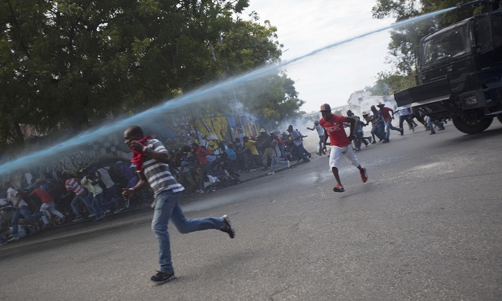 People run for cover as police spray water into a crowd of protesters calling for the resignation of President Michel Martelly, in Port-au-Prince, Haiti, Saturday, Jan. 10, 2015.