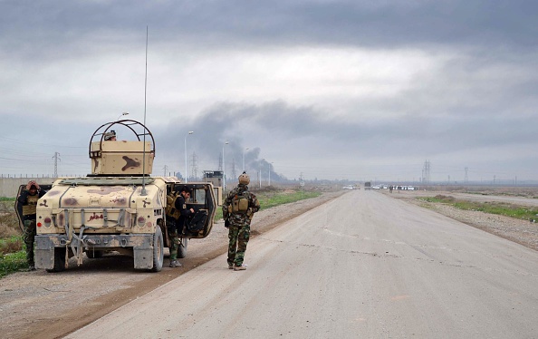 Smoke billows in the background as Kurdish Peshmerga fighters take positions on the side of a road in the northern Iraqi city of Kirkuk on January 30, 2015. 