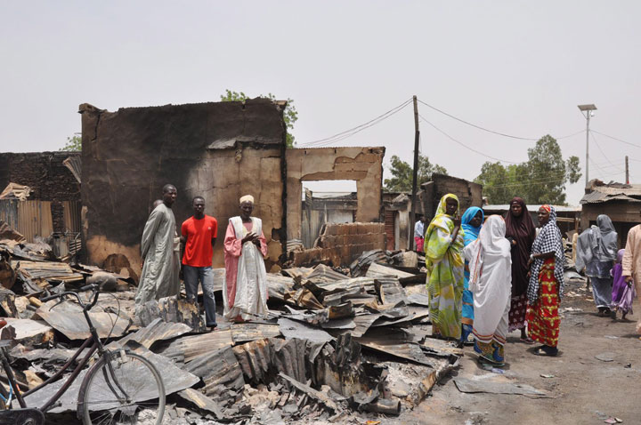 In this Sunday, May 11, 2014 file photo, people stand outside burnt houses following an attack by Islamic militants in Gambaru, Nigeria. Cameroon's government said Tuesday that its military killed 143 militants from the Islamic extremist group Boko Haram, which has been waging war in neighbouring Nigeria. 