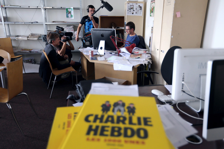 French satirical weekly Charlie Hebdo's publisher and cartoonist, known as Charb (R), works at his desk on an issue which features a satirical drawing he drew, entitled 'Intouchables 2', while journalists are filming an recording, on September 19, 2012 at the weekly's headquarters in Paris. 
