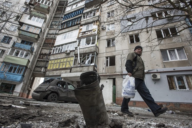 A man walks by a burned car and a piece of exploded Grad missile, outside an apartment building in Vostochniy district of Mariupol, Eastern Ukraine, Sunday, Jan. 25, 2015. (AP Photo/Evgeniy Maloletka).