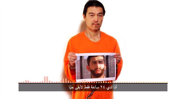 This still image taken from a video posted on YouTube by jihadists on Tuesday, Jan. 27, 2015, shows a still photo of Japanese journalist Kenji Goto holding what appears to be a photo of Jordanian pilot 1st Lt. Mu'ath al-Kaseasbeh. Both are being held hostage by the Islamic State militant group. The Associated Press could not independently verify the video. (AP Photo).