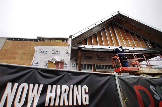 FILE - In this Jan. 12, 2015 file photo, a now hiring sign hangs nearby as a builder works on a commercial property under construction in Peabody, Mass.
