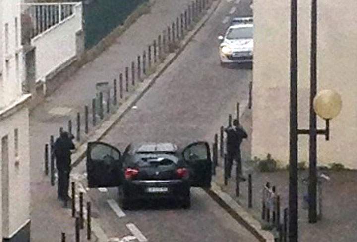 Armed gunmen face police officers near the offices of the French satirical newspaper Charlie Hebdo in Paris on Jan. 7.