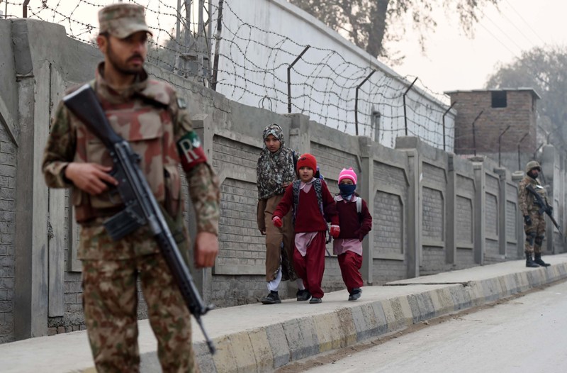Pakistani soldiers stand guard on a street as children walk to school in Peshawar on January 12, 2015. Schools in Pakistan's northwestern city of Peshawar re-opened on January 12 for the first time since a Taliban raid massacred 150 people, mainly children, with returning students expressing defiance tinged with apprehension. 