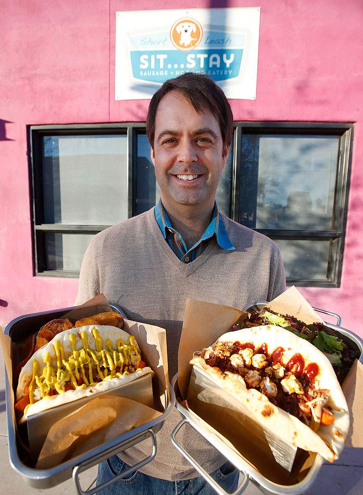 In this Jan. 14, 2015 photo, Short Leash SitÖStay restaurant co-owner Brad Moore holds up two of their hotdog menu items, the Bear, right, and the Chicago in Phoenix. The Super Bowl takes place Feb. 1 in nearby Glendale, Ariz., and the restaurant scene in downtown Phoenix sees the game as an opportunity to show off its creative local cuisine.