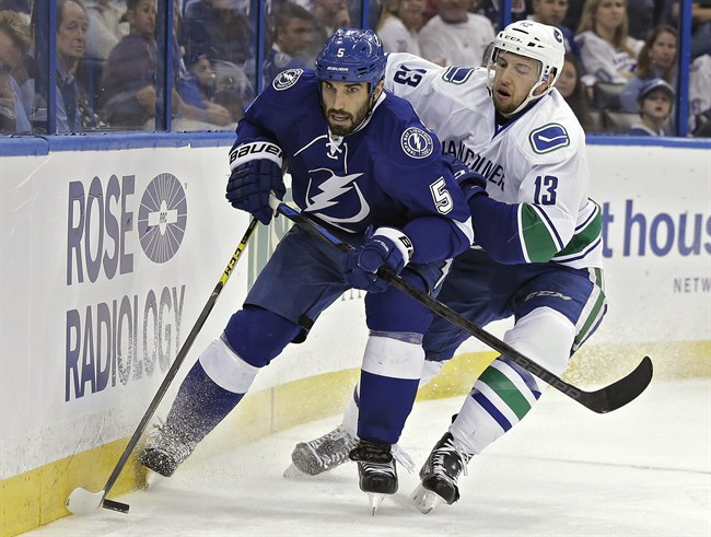 Tampa Bay Lightning defenseman Jason Garrison (5) beats Vancouver Canucks center Nick Bonino (13) to a loose puck behind the goal during the first period of an NHL hockey game Tuesday, Jan. 20, 2015, in Tampa, Fla. 
