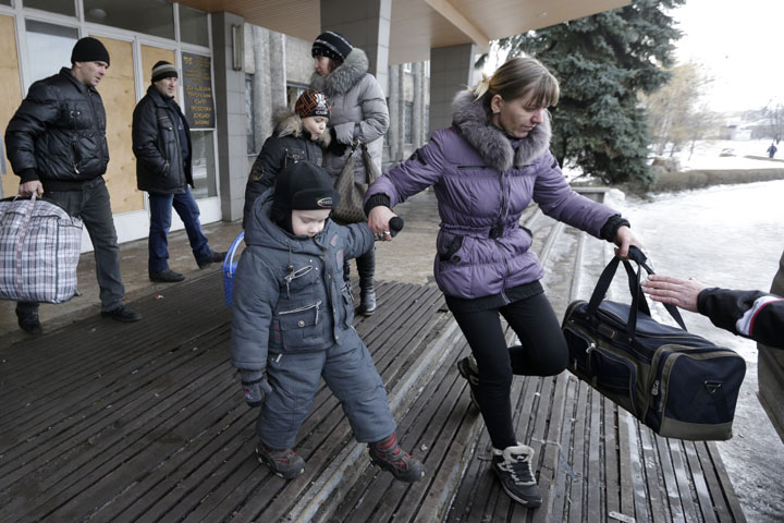 People carry their belongings as they walk to a bus to leave the town of Debaltseve, Ukraine, Saturday, Jan. 31, 2015.
