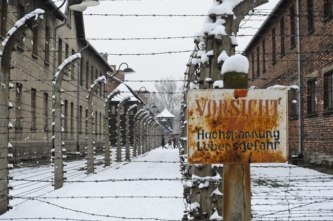 Visitors walk between barbed wire fences at the Auschwitz Nazi death camp in Oswiecim, Poland, Monday, Jan. 26, 2015. Poland's president has signed legislation that outlaws blaming Poland as a nation for Holocaust crimes committed by Nazi Germany.