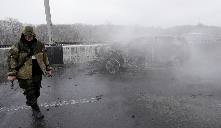 A Pro-Russian rebel walks past a car destroyed by a rocket during recent shelling in Donetsk, Ukraine, Monday, Feb. 9, 2015.