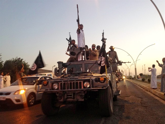 In this photo taken Monday, June 23, 2014, fighters from the Islamic State group parade in a commandeered Iraqi security forces armored vehicle down a main road in the northern city of Mosul, Iraq.