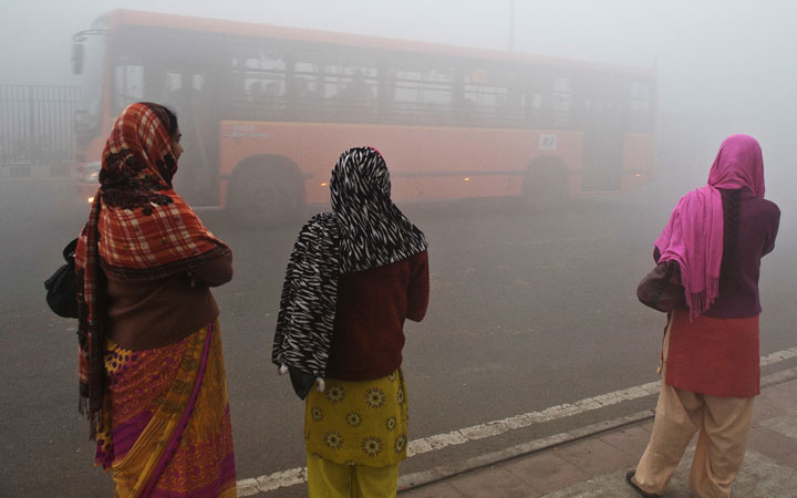 Indian commuters wait for a bus early on a polluted morning in New Delhi on January 31, 2013.