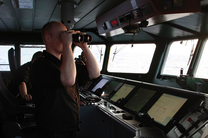 In this Jan. 14, 2015 photo, Lt. Martin Sovang, of the Icelandic Coast Guard ship Tyr, uses binoculars to scan the horizon in the waters between Greece and Italy. The ship is part of the 19-nation Operation Triton patrolling the seas for the rising numbers of migrants. 