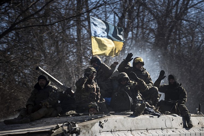 Ukrainian troops wave as they ride on an armoured vehicle, with a Ukrainian flag atop, near Artemivsk, eastern Ukraine, Tuesday, Feb. 24, 2015. 