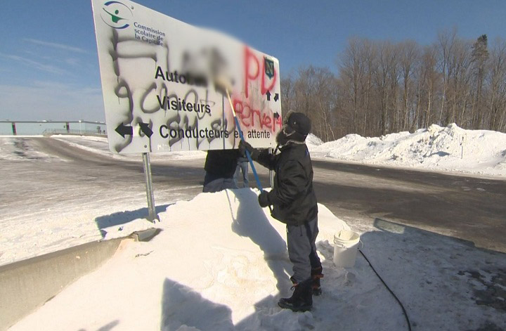 A worker removes graffiti from a sign outside Neufchatel High School in Quebec City after a 15-year-old student was strip searched by school authorities in February 2015.