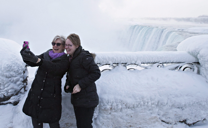 Visitors Rosalie Vissers, left, and Rachel Houter take a photo near masses of ice formed around the falls.