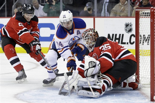 Edmonton Oilers right wing Jordan Eberle (14) tries to get the puck past New Jersey Devils defenseman Adam Larsson (5), of Sweden, and goalie Cory Schneider (35) during the first period of an NHL hockey game Monday, Feb. 9, 2015, in Newark, N.J. (AP Photo/Mel Evans).