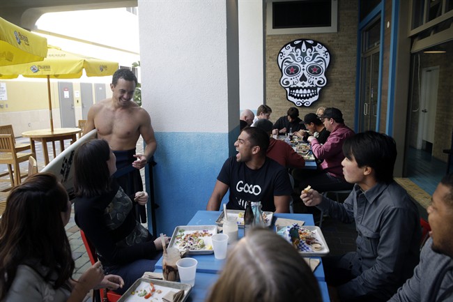 In this Feb. 20, 2015 photo, Nathan Seymour, top left, with a surfboard, chats with his friends at U.S. Taco Co., which is owned by Taco Bell, in Huntington Beach, Calif. As people increasingly reach for foods that stray from the norm and seem less processed, some companies are testing whether it would pay to tuck away their famous logos in favor of more hipster guises. (AP Photo/Jae C. Hong).