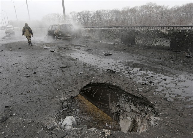 A Pro-Russian rebel walks past a car destroyed by a rocket during recent shelling in Donetsk, Ukraine, Monday, Feb. 9, 2015. 