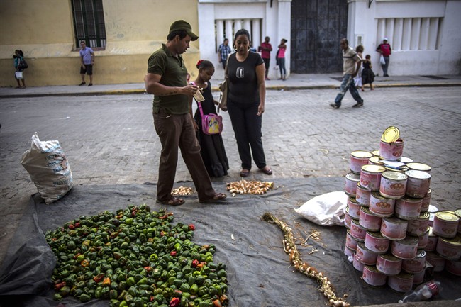 A vegetable street vendor who sells bell peppers, garlic and cans of crushed tomatoes, attends to a woman and her daughter in Old Havana, Cuba, Tuesday, Feb. 17, 2015.