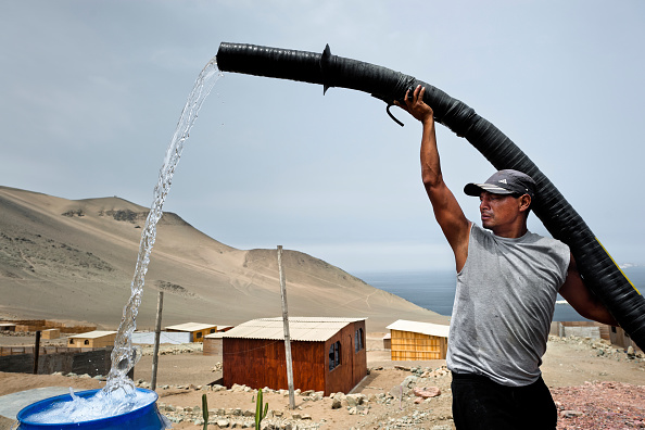 A Peruvian water distribution worker with a pipe fills a tank with drinking water on the dusty hillside of Pachacútec, a desert suburb, on January 21, 2015 in Lima Peru. 