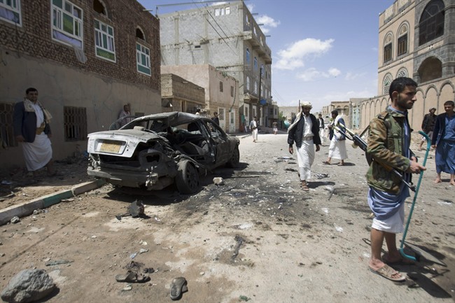 Shiite rebels, known as Houthis, stand near a damaged car after a bomb attack in Sanaa, Yemen, Friday, March 20, 2015.