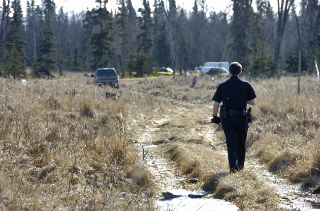 A Kenai police officer walks down a trail leading to a temporary camp where police and Federal Bureau of Investigations personnel Sunday, March 22, 2015 are working to identify remains of what Kenai Police believe to be a family who have been missing for nearly 10 months from their Kenai, Alaska home. 