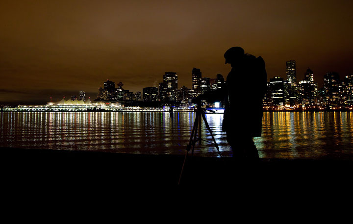 A woman takes photographs after many downtown buildings turned their lights off during Earth Hour in Vancouver, B.C., on Saturday March 31, 2012.
