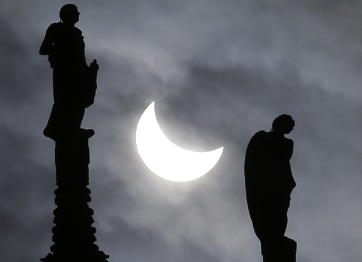 The sun is seen during an eclipse between two statues of the Duomo gothic cathedral in Milan, Italy, Friday, March 20, 2015.