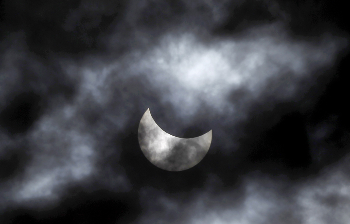 The moon starts to block the sun during a solar eclipse seen through clouds, in Skopje, Macedonia, Friday, March 20, 2015.