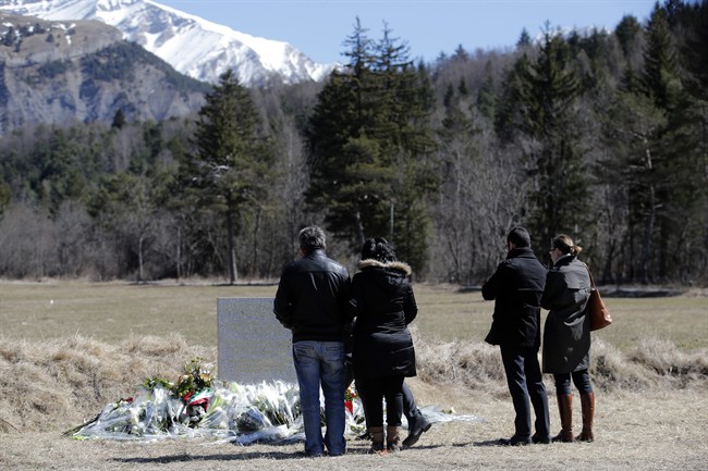 People and family members of a victim pay tribute next to a stele and flowers laid in memory of the victims in the area where the Germanwings jetliner crashed in the French Alps, in Le Vernet, France, Friday, March 27, 2015. The crash of Germanwings Flight 9525 into an Alpine mountain, which killed all 150 people aboard, has raised questions about the mental state of the co-pilot. Authorities believe the 27-year-old German deliberately sought to destroy the Airbus A320 as it flew Tuesday from Barcelona to Duesseldorf. 