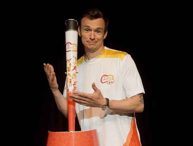 Olympian Simon Whitfield poses with the official Pan Am torch and uniforms in Toronto on Monday, March 16, 2015.