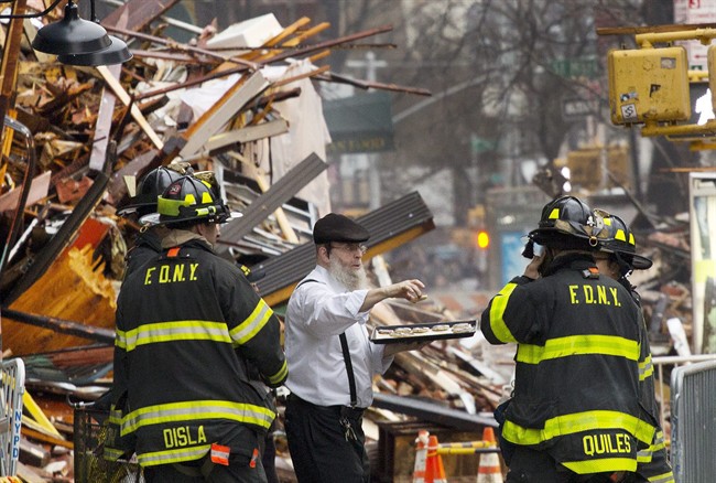 A man distributes pastries to weary firefighters at the site of an explosion and fire in the East Village neighborhood of New York, Friday, March 27, 2015.