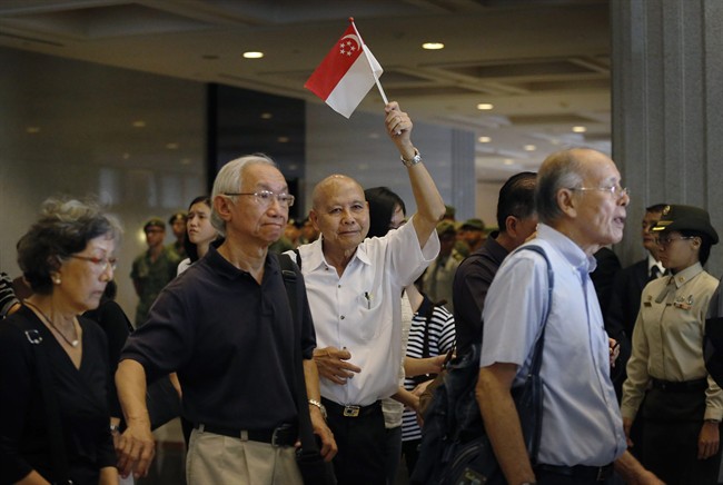 A man holds up the national flag of Singapore as others grieve while paying respects to the late Lee Kuan Yew at the Parliament House where he will lie in state for four days, Wednesday, March 25, 2015.