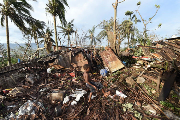 Samuel, only his first name given, kicks a ball through the ruins of their family home as his father, Phillip, at back, picks through the debris in Port Vila, Vanuatu in the aftermath of Cyclone Pam Monday, March 16,.