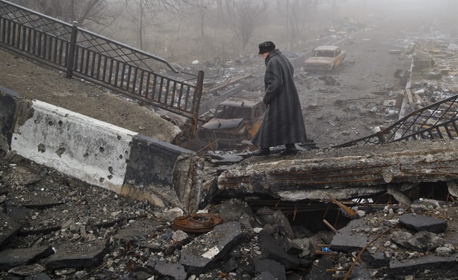 An elderly woman walks across a destroyed bridge, fallen onto the road towards the airport, the scene of heavy fighting in Donetsk, Ukraine, Sunday, March 1, 2015. The recent pullback of some weapons from the line separating government and rebel forces in Ukraine seems to have boosted the prospects for peace, although both sides are warning of their readiness to resume fighting if necessary. 