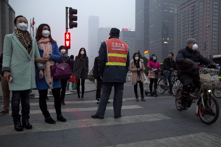 Pedestrians wearing mask against heavy pollution wait to cross a traffic junction in Beijing, Monday, March 16, 2015. 