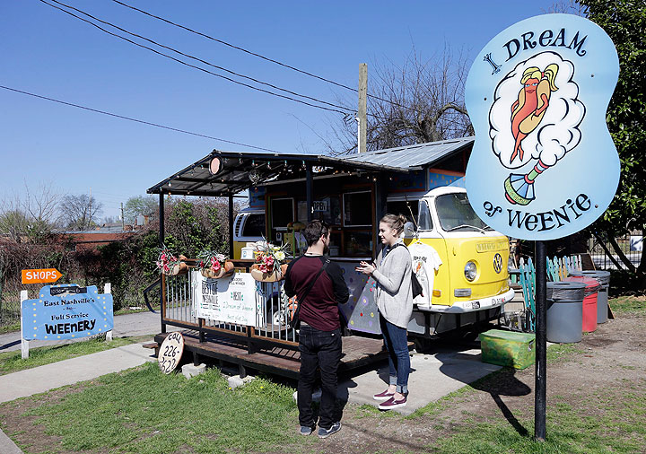 In this April 4, 2015, photo, customers visit the I Dream of Weenie hot dog stand, housed in a Volkswagen Microbus, in the East Nashville area of Nashville, Tenn. East Nashville houses an eclectic collection of restaurants, bars, coffee shops, bakeries and stores, mixed into a residential area of 1950s and 1960s homes.