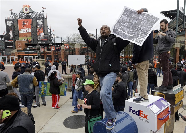 A protestor stands on a mailbox outside of Oriole Park at Camden Yards before a baseball game between the Boston Red Sox and the Baltimore Orioles after a rally for Freddie Gray, Saturday, April 25, 2015, in Baltimore. 