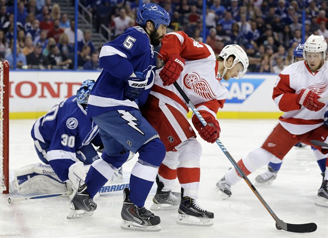 Detroit Red Wings center Gustav Nyquist, center, tries to back in on Tampa Bay Lightning defenseman Jason Garrison (5) during the first period of Game 7 of a first-round NHL Stanley Cup hockey playoff series Wednesday, April 29, 2015, in Tampa, Fla.