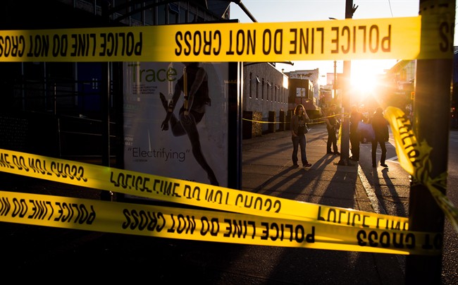 Police officers are framed by police tape as they work at the scene where they shot and killed a man who allegedly stabbed three people in the Downtown Eastside of Vancouver, B.C., on Thursday April 9, 2015. 