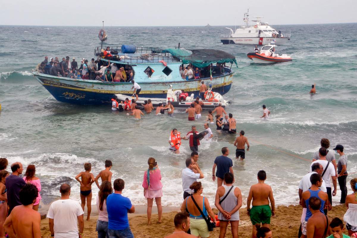 In this Aug. 15, 2013 file photo, Italian Coast Guard officers and holiday-makers help migrants to get off a boat near Siracusa, Italy.