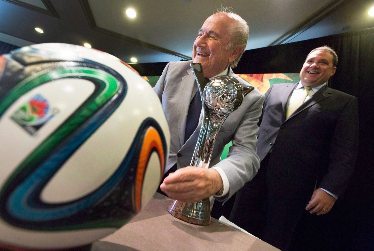 FIFA President Sepp Blatter, left, pretends to shine the trophy with his suit jacket sleeve while posing for photographs with Canadian Soccer Association President Victor Montagliani following the opening press conference for the FIFA Women's Under 20 World Cup in Toronto, Ontario on Monday, Aug. 4, 2014. 